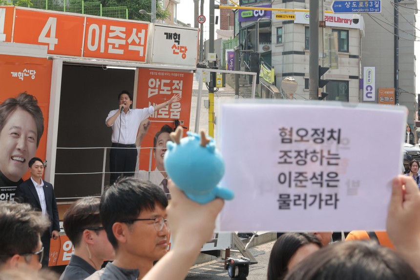 개혁신당 이준석 대선 후보가 지난달 30일 서울 동작구 중앙대학교에서 유세 중인 가운데 일부 학생들이 최근 이 후보의 TV토론 여성 신체 관련 발언을 규탄하며 팻말을 들고 있다. 연합뉴스