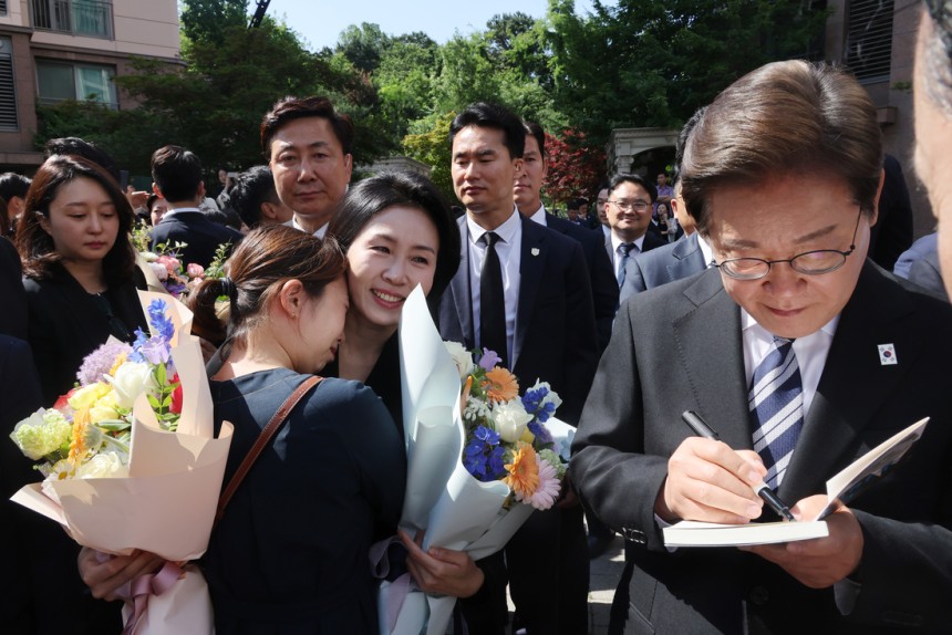 이재명 대통령과 김혜경 여사가 4일 인천 계양구 사저를 출발하다 이 대통령이 책에 서명을, 김 여사가 한 주민과 포옹을 하고 있다. 연합뉴스