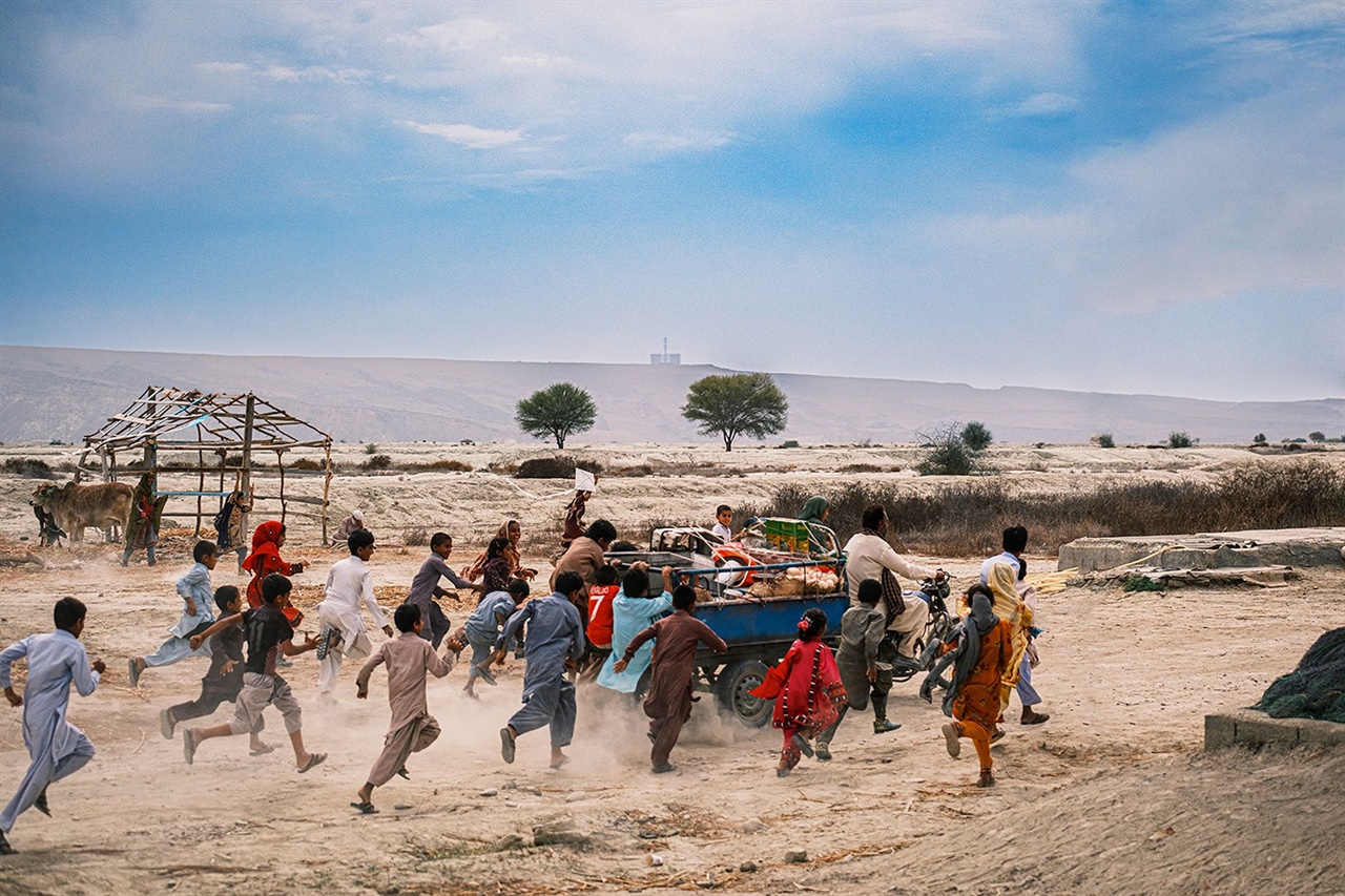 イランの村で子どもたちが食料を積んだ車を追いかける映画『パンと本』の場面