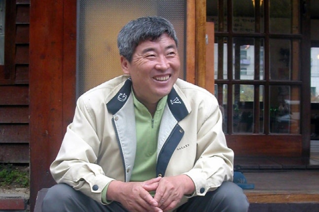 木造の建物の前で笑顔を見せる作詞家チャン・ギョンスさん(写真提供:大衆音楽評論家パク・ソンソ/聯合ニュース)