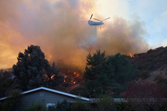 On January 11 (local time), a firefighting helicopter sprays water over houses near the site of the wildfire raging for the fifth day in Los Angeles (LA) area, U.S. West. 2025.1.11 EPA Yonhap News