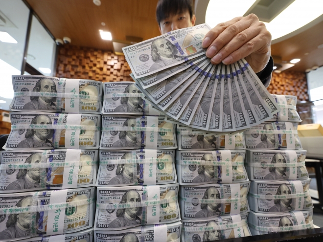 16일 서울 중구 하나은행 위변조대응센터에서 직원이 미화 100달러 뭉치를 정리하며 1300달러를 펼쳐 보이고 있다.외환당국은 환율 안정을 위해 국민연금과 650억 달러 규모의 외환스와프 계약을 내년까지 1년 연장