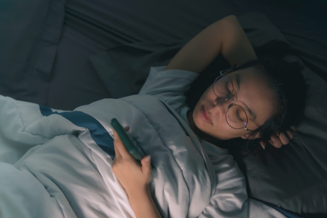 한 여성이 침대에 누워 스마트폰을 하는 모습(기사와 직접적 관련 없음).123RF