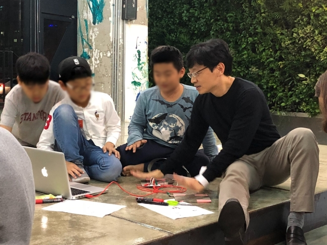 권혁빈(오른쪽 첫번째) 스마일게이트 최고비전제시책임자(CVO)가 최근 경기 성남시 분당구 본사에서 열린 퓨처랩 행사에서 초등학생들이 만든 코딩 프로젝트를 살펴보며 이야기를 나누고 있다. 스마일게이트 지분 100%를 