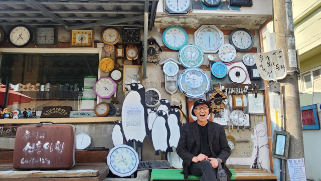 광주 양림동 펭귄마을 촌장 김동균 씨가 가장 애착 가는 펭균마을 내 시계 거리에서 환하게 웃고 있다. 13년 전부터 쓰레기들을 주워 모아 펭균마을을 조성한 김 촌장의 노력으로 이곳은 연간 20만 명이 찾는 명소가 됐