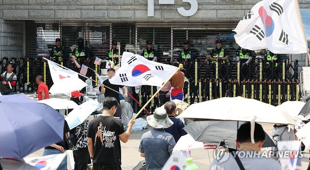 ◇6·3 지방선거 당시 잠실 개표소로 사용된 서울 송파구 올림픽공원 핸드볼경기장 앞에서 지난 6월 28일 투표용지 부족 사태 규탄 봉쇄 시위 참가자들이 우산을 쓰고 구호를 외치고 있다. 2026.6.28. 연합뉴스.