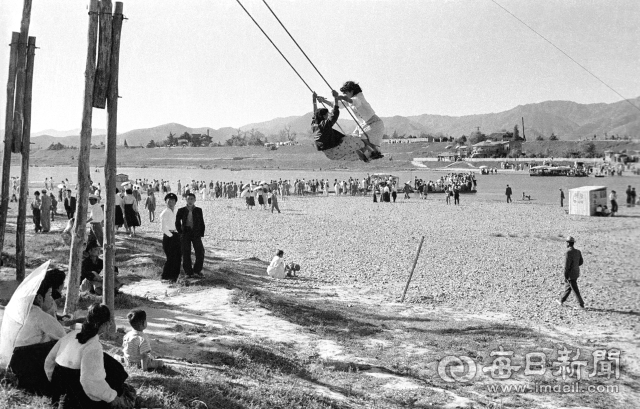 1959년 6월 10일 단오날을 맞아 동촌 유윈지에 나들이 온 두 아낙네가 쌍그네를 타고 있다.멀리 강변에 줄지어 선 사람들은 강을 건너기 위해 나룻배를 기다리는 모습이다.사진=매일아카이빙센터