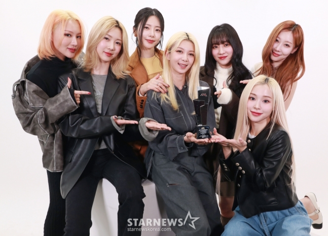 Dreamcatcher poses in casual clothes indicating their Asia Artist Awards trophy, held by Dami.