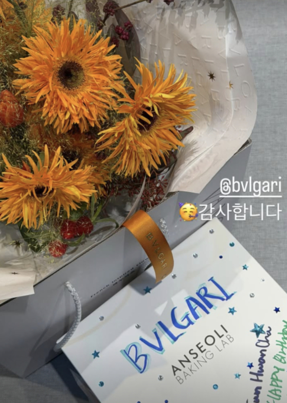 ブルガリのロゴ入りギフトバッグとオレンジ色の花束を写したチャ・ジュンファンの投稿写真