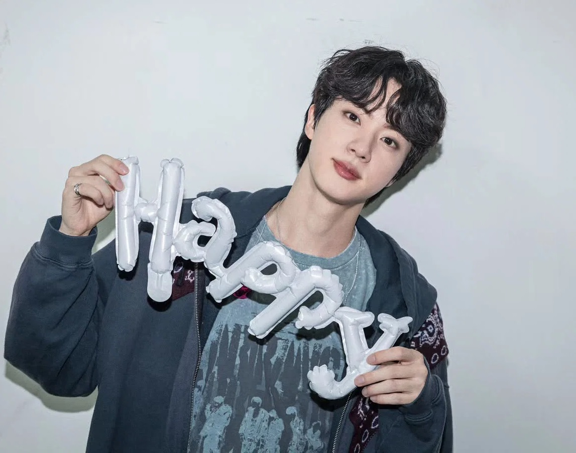 「Thank You」の文字を持ち、笑顔を見せるBTSのジン