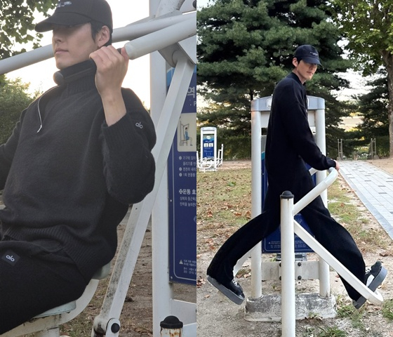 黒い帽子と服を着たキム・ウビンが、公園の屋外運動器具を使う様子。