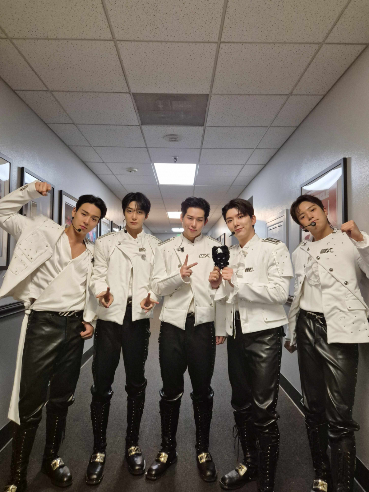 白いステージ衣装を着たMONSTA Xのメンバーが、廊下で並んでポーズを取る