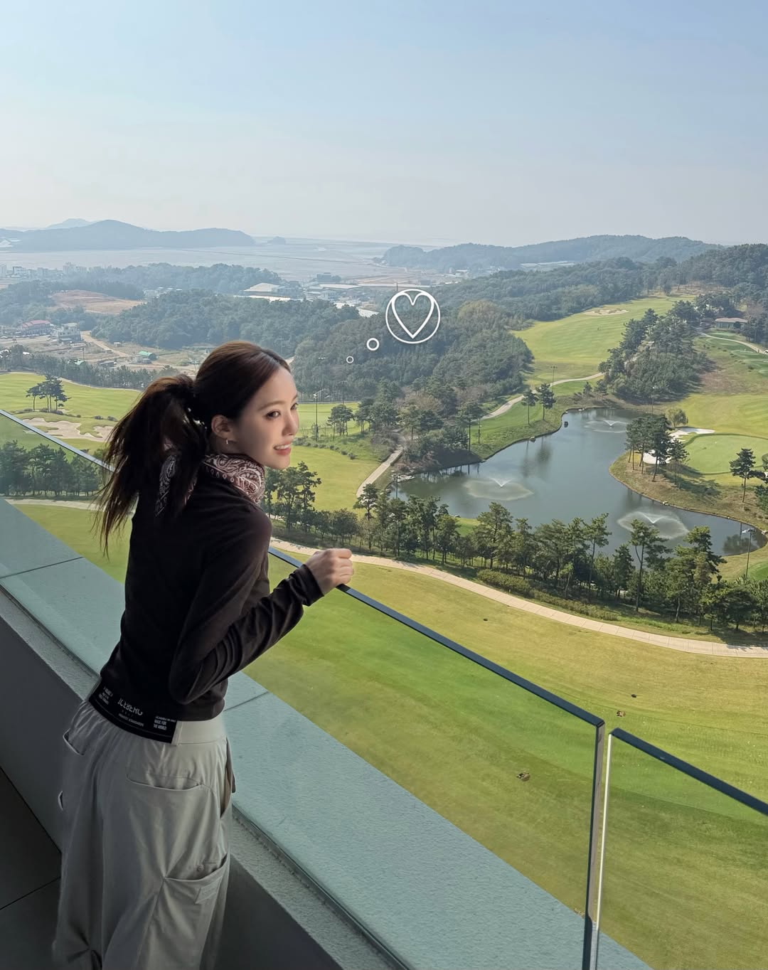湖と緑のフィールドを背景に、手すりに寄りかかるヒョミン