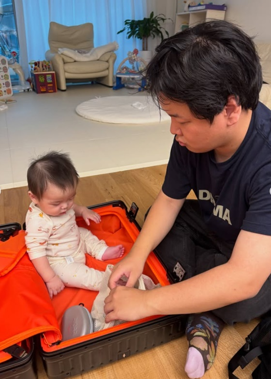 旅行の荷造りをするクァクチューブのそばで、オレンジ色のスーツケースに座る息子
