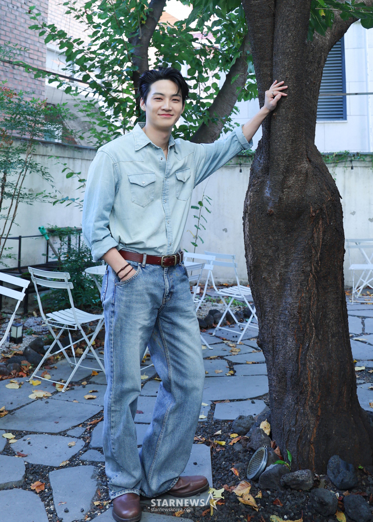 薄いデニムシャツとジーンズを着て、木のそばでポーズを取るJAY B