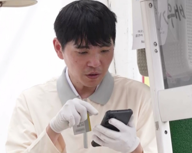 配達スタッフの制服と手袋姿で、手元の端末を確認するイ・セドル