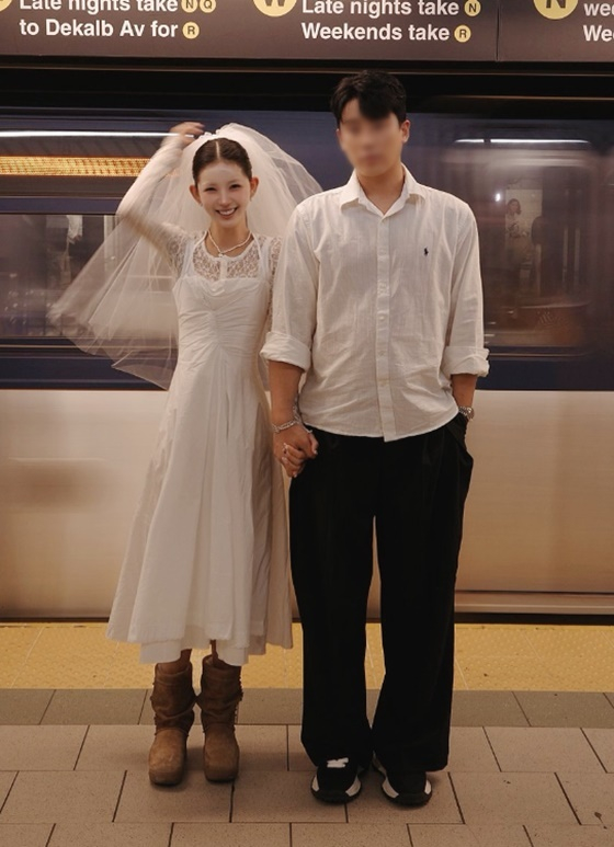 ニューヨークの街角でウェディングドレスとベールを身につけたチェ・ジュンヒが夫と並ぶ写真