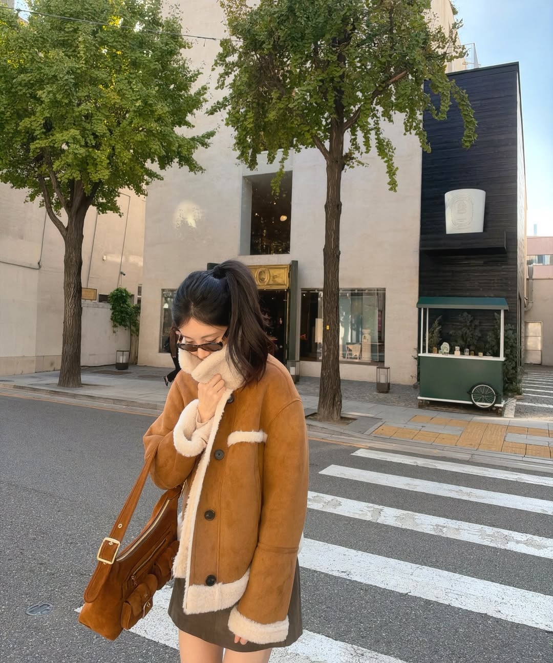 茶色のムートン風ジャケットとミニスカート、ロングブーツ姿で街を歩くソヒョン