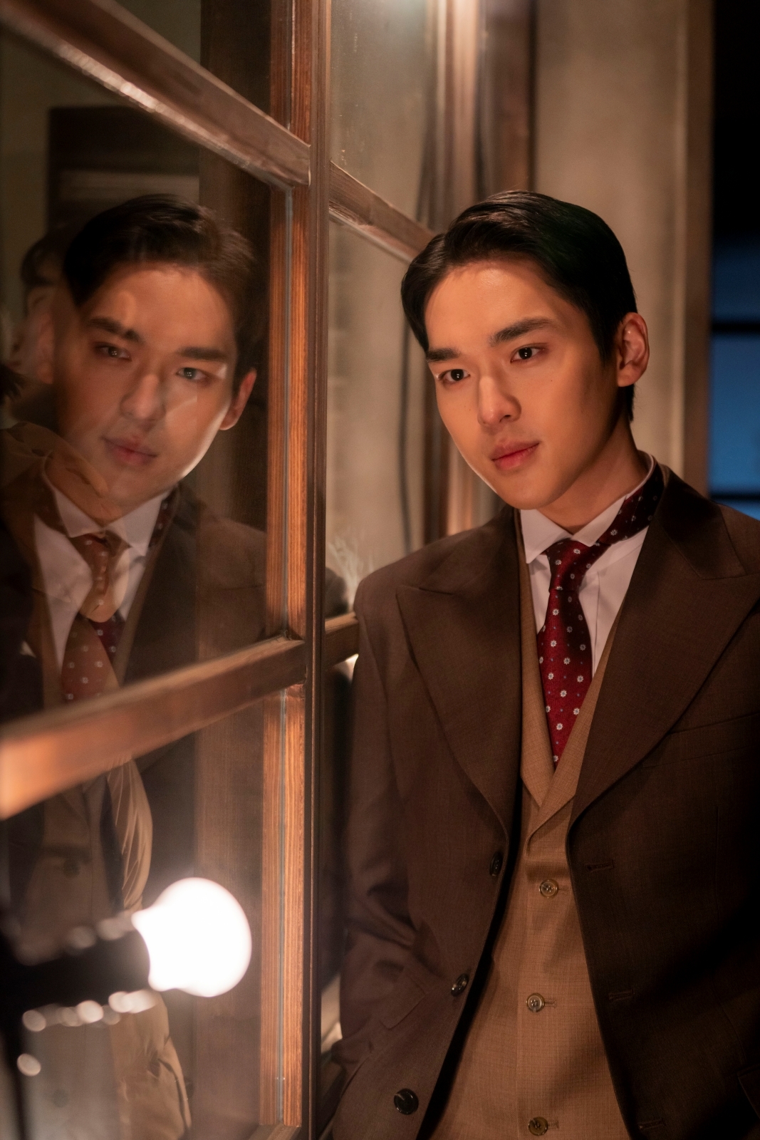 映画『今もなお、輝かしく』でドゥヨンを演じるムン・ソンヒョン。窓に映る姿とともに写っている。