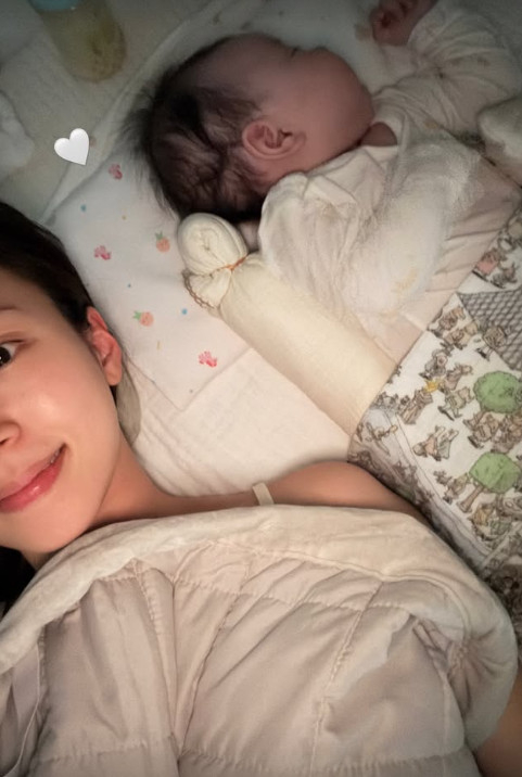 布団の中でカメラを見つめるキム・ジヨンと、隣で眠る娘