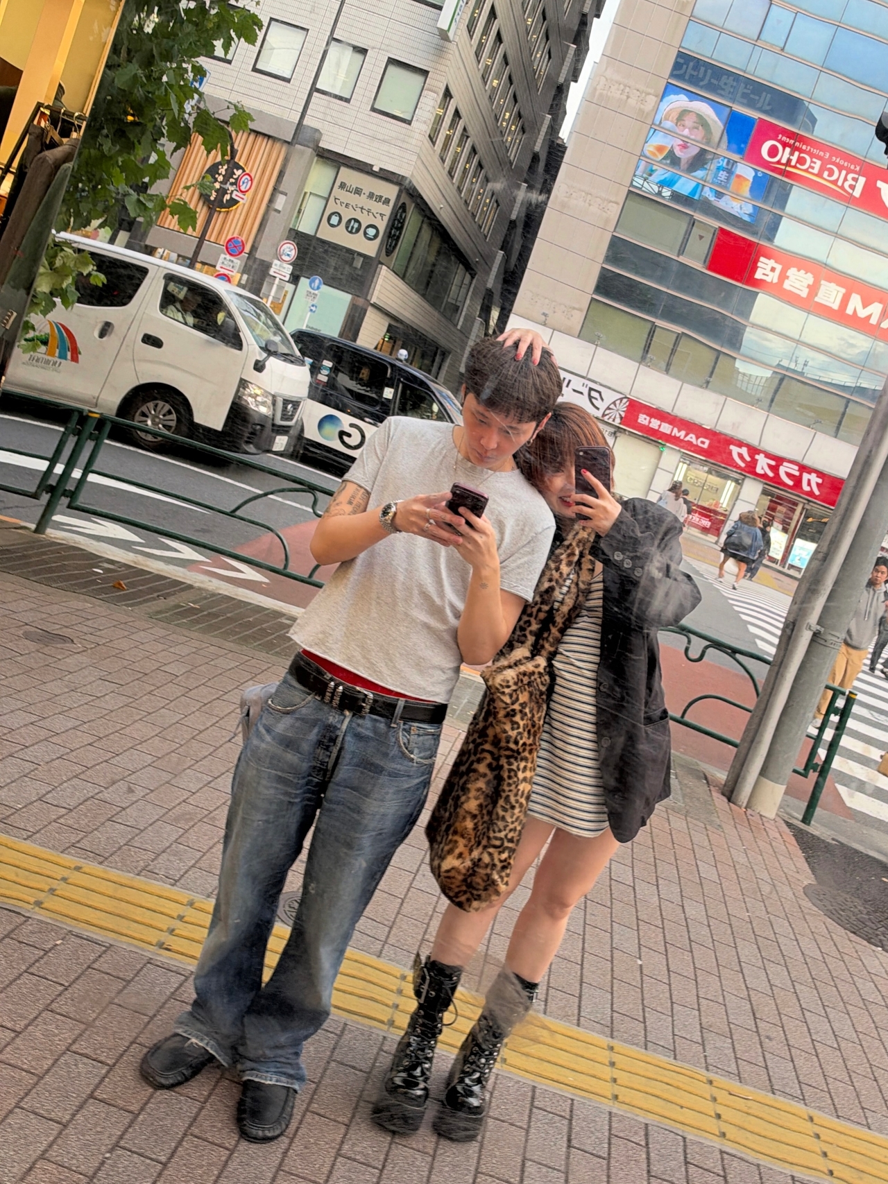 日本の街中で、鏡に映った姿をスマートフォンで撮影するヒョナとヨン・ジュニョン。