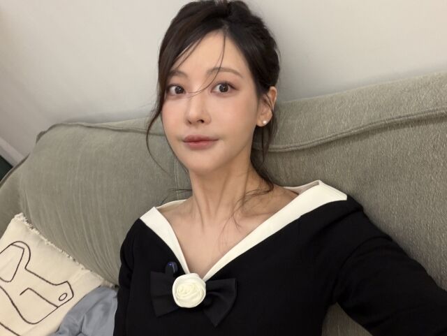 白い襟と大きな黒いリボン飾りの服を着て、ソファでセルフィーを撮るオ・ヨンソ