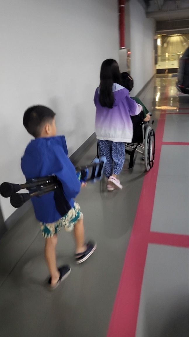손녀는 할머니 휠체어를 밀고, 손자는 목발을 들고 가는 모습 ⓒ