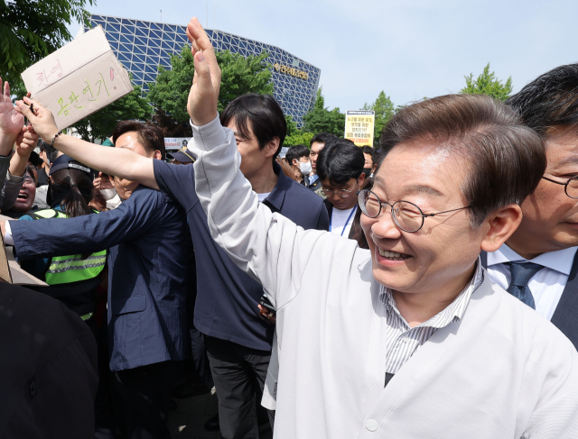 더불어민주당 이재명 대선 후보가 '골목골목 경청투어:국토종주편'에 나선 7일 전북 전주시 풍남문 앞 광장에서 지지자가 든 공판 연기 환영 팻말을 지나고 있다.이날 서울고등법원은 오는 15일 예정됐던 이 후보의 공직