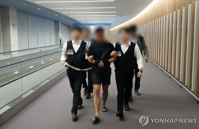 법무부 관계자들이 그룹 방탄소년단(BTS) 정국을 포함한 국내 재력가들의 명의를 도용해 거액을 빼돌린 해킹조직 총책급 범죄인인 중국 국적 전모씨를 인천국제공항을 통해 강제송환하고 있다. [사진=연합뉴스]