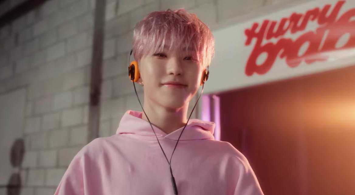 SEVENTEEN's Hoshi in the 'Agyochak' music video with pink hair, looking charming in a studio setting.