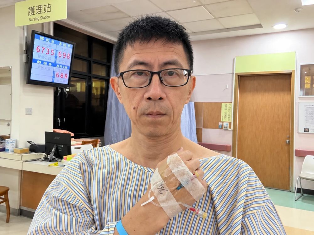 病院の患者衣を着て腕に点滴の針をつけた台湾歌手リー・ジー