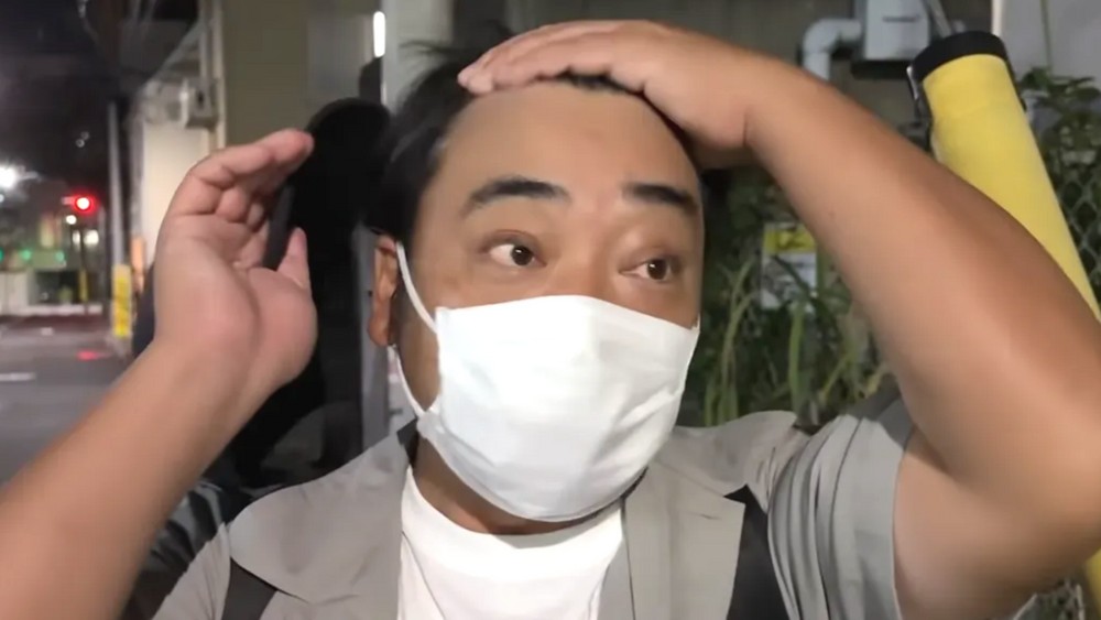 白いマスクを着け、頭に手を添える斉藤慎二