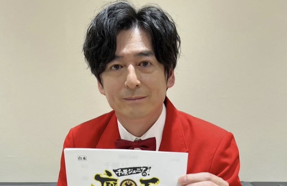 赤いジャケット姿で番組の資料を手にする博多大吉