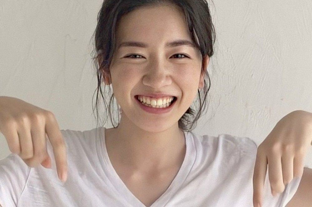 白いTシャツ姿で笑顔を見せ、両手で下を指す永野芽郁