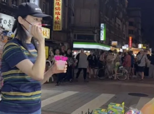 帽子とマスク姿で台北の夜市を歩き、飲み物を手にするジェン・シュアン