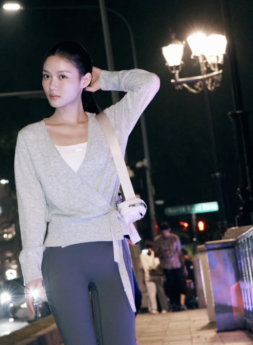 グレーのトップスと濃い色のパンツを合わせ、白いバッグを肩に掛けたキム・ユジョン
