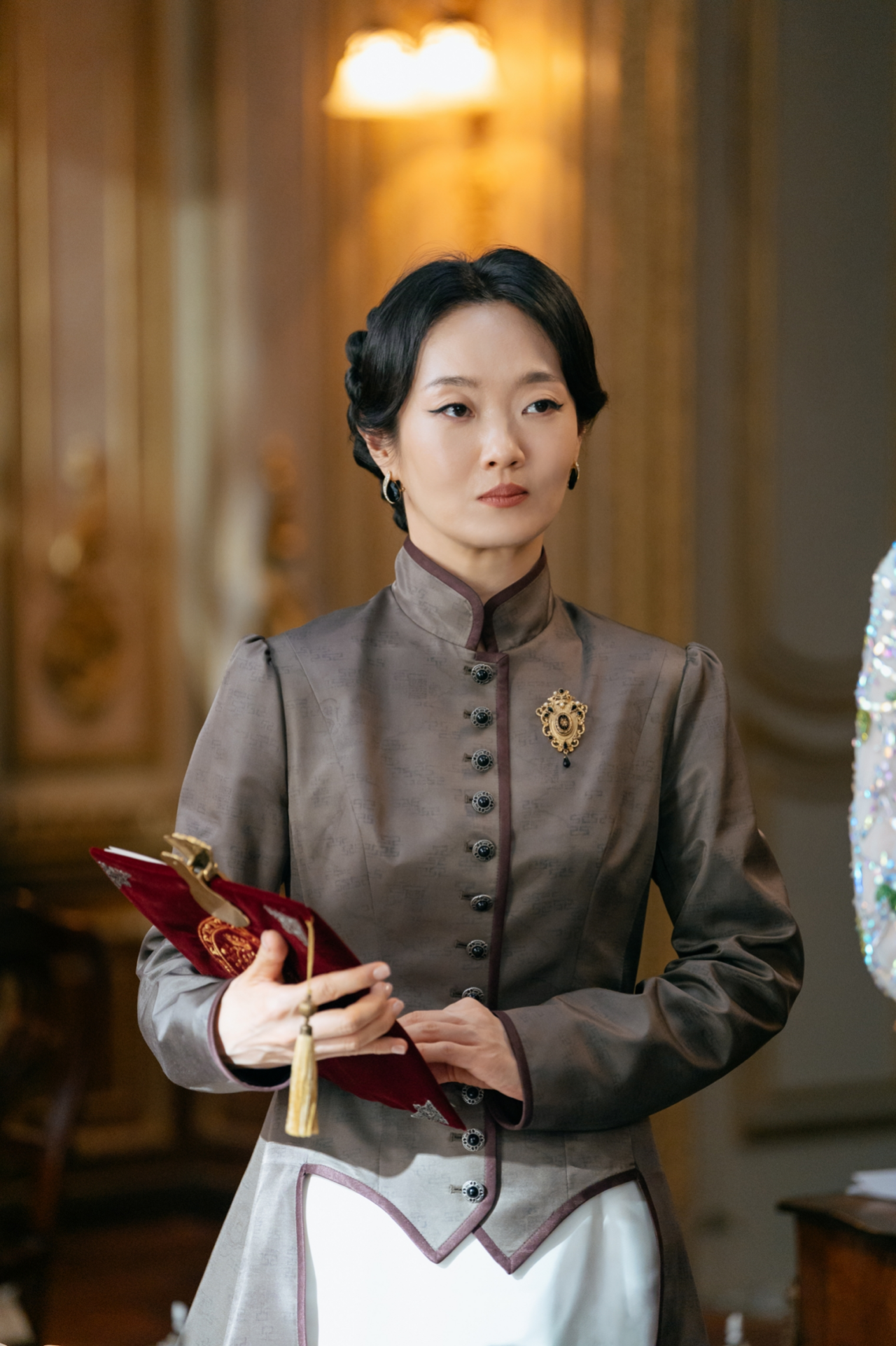 『再婚皇后』で西宮の女官長エリザを演じるイ・ボンリョン。灰色の衣装をまとい、手にした赤い帳面を見つめる