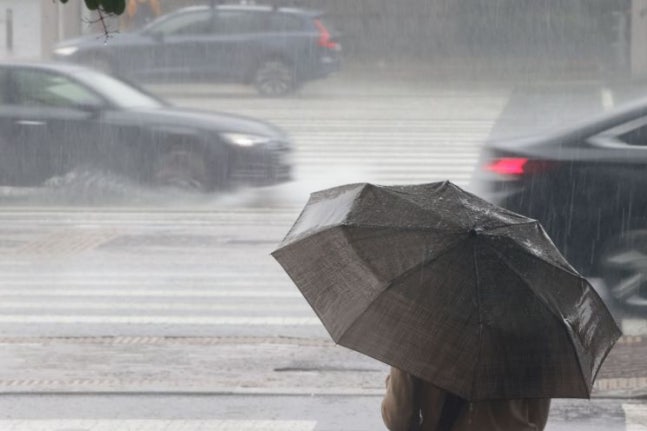 A citizen standing to cross a crosswalk in the pouring rain. [Image Source= Yonhap News]