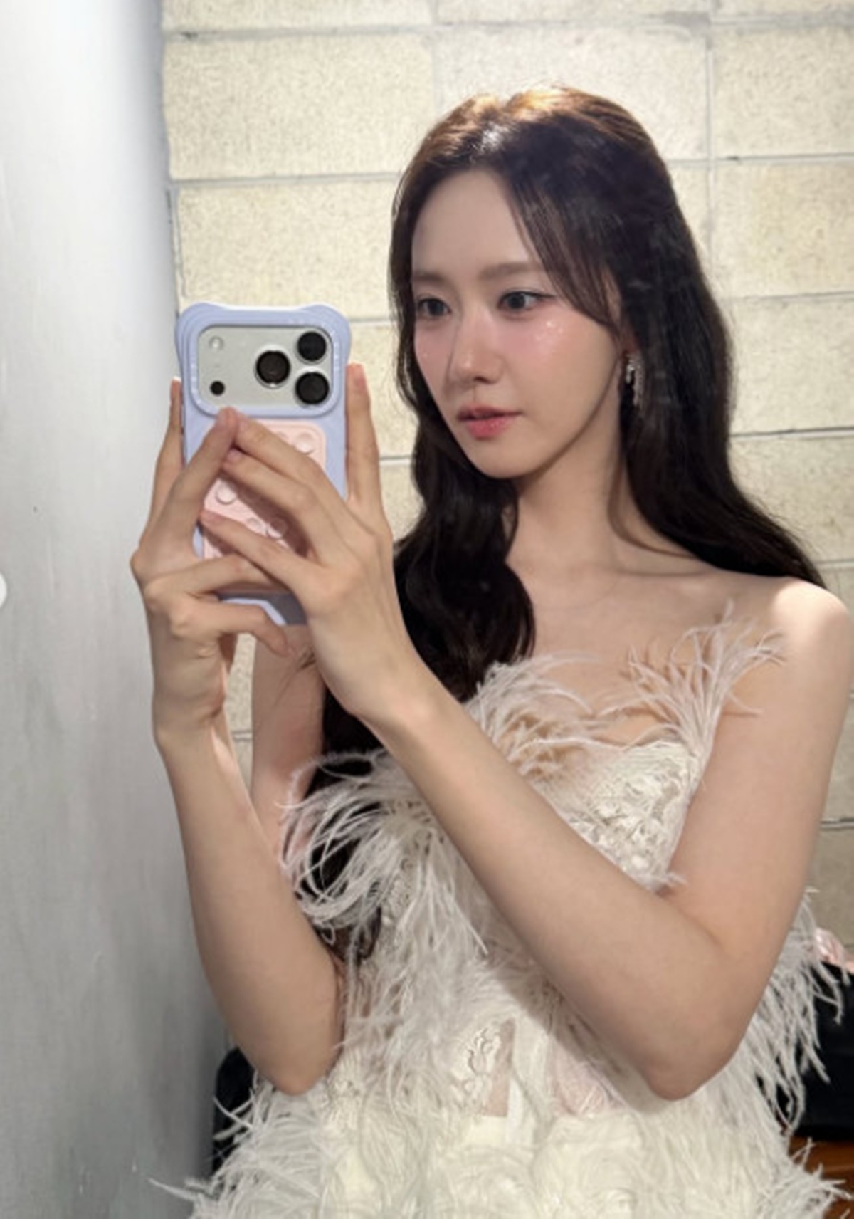 白い羽根飾りのチューブトップドレス姿でスマートフォンを手に撮影する少女時代ユナ