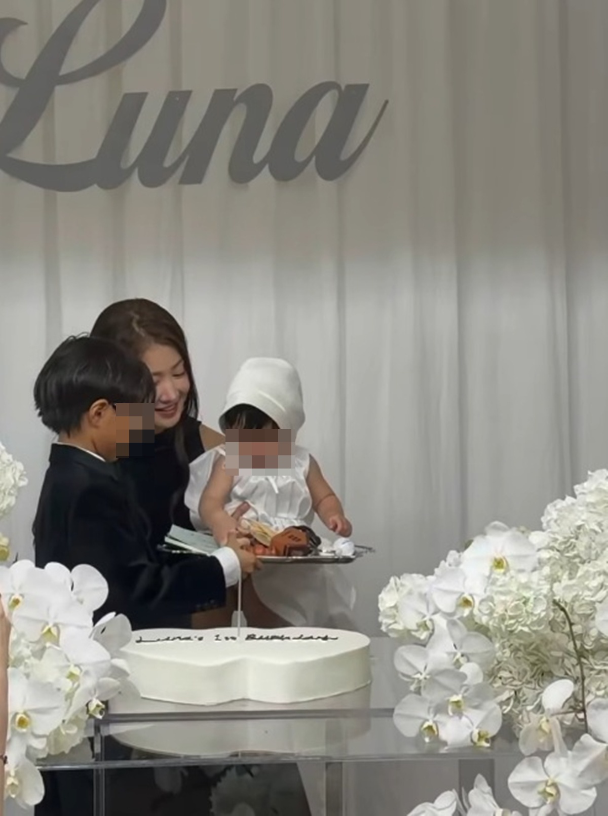 白い衣装の娘と黒いタキシード姿の息子を囲み、誕生日ケーキの前に立つイ・シヨン