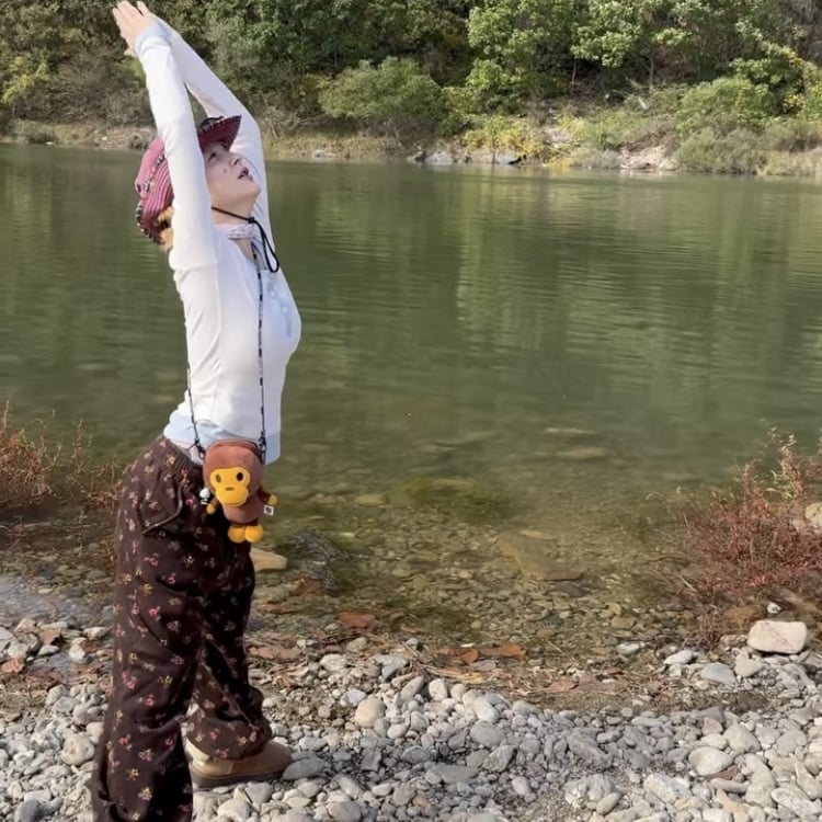 川辺で両腕を伸ばすAOA出身ジミン。ピンクの帽子と柄入りのパンツを着用している