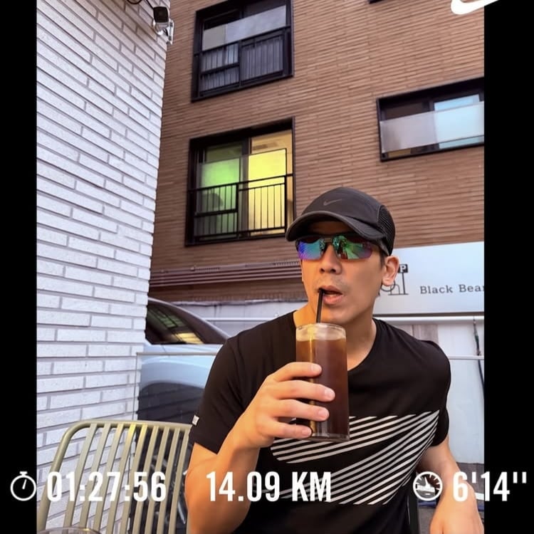 黒い運動着姿で飲み物を手にする28期クァンスさん。画像には14.09kmのランニング記録も表示されている