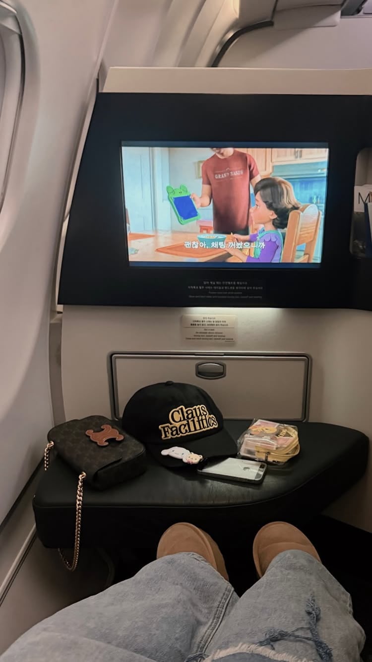 済州島へ向かう機内のビジネスクラス席。テーブルに荷物が置かれ、座席前のモニターが映っている