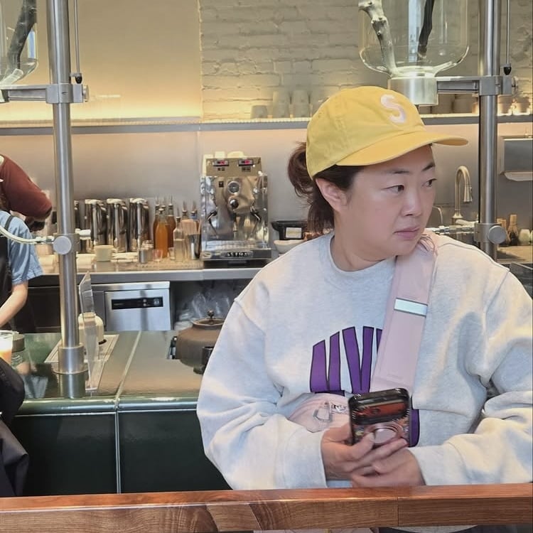 ニューヨークの店内で黄色い帽子をかぶり、スマートフォンを手にする22期チョンスク