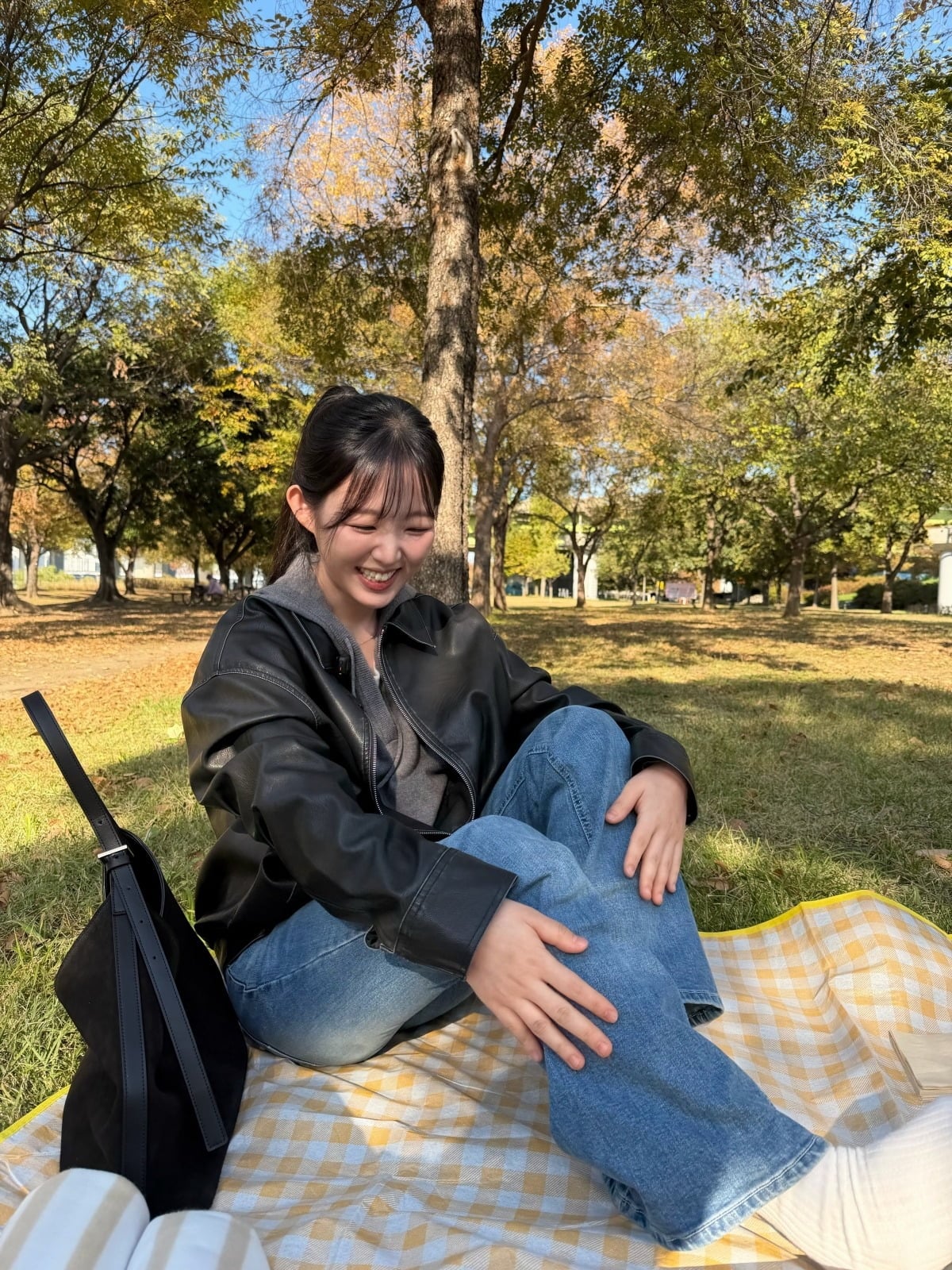 秋色に染まった公園で、黒いレザージャケット姿のキム・シヒョンが笑顔を見せる