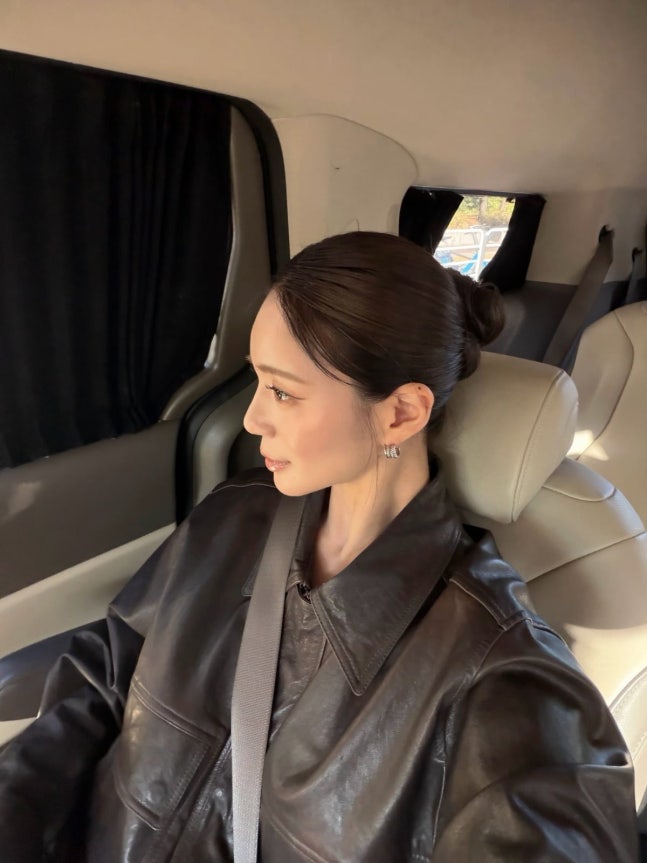 車の後部座席で窓の外を見るイ・エリヤ。髪を後ろでまとめ、黒いレザージャケットを着ている