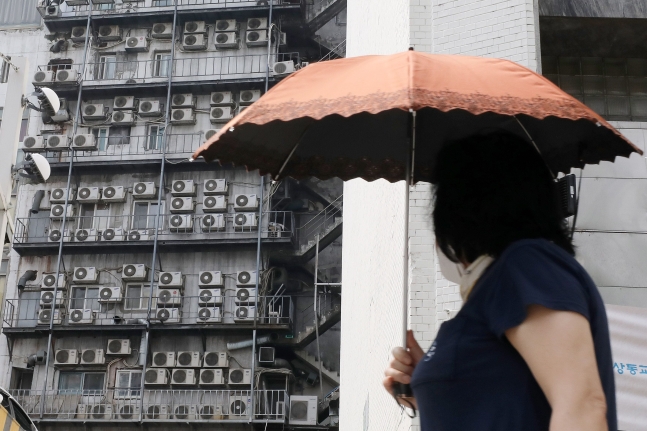 서울 시내 한 건물 외벽에 가득 매달린 에어컨 실외기 앞으로 양산을 쓴 시민이 지나가고 있다. /뉴스1