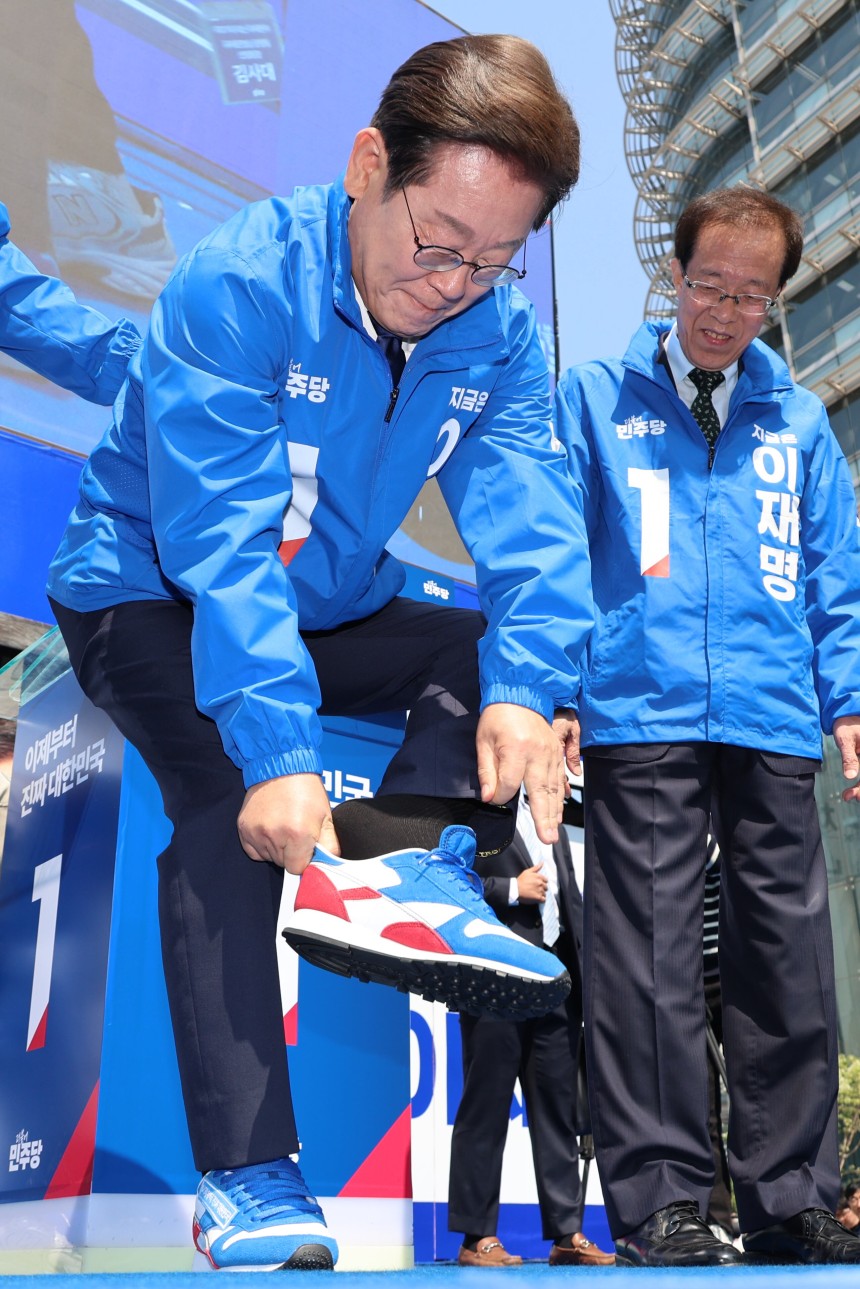 이재명 더불어민주당 대선 후보가 제21대 대선 공식 선거 운동 첫날인 12일 서울 광화문 청계광장에서 열린 중앙선대위 출정식에서 구두를 벗고 청색, 적색이 섞인 운동화로 갈아 신고 있다. /연합뉴스