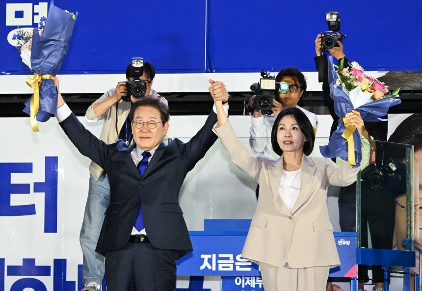 제21대 대통령 당선이 확실시되는 더불어민주당 이재명 대선 후보와 부인 김혜경 여사가 4일 서울 여의도 국회 인근에서 당 주최로 열린 국민개표방송 행사에 참석해 꽃다발을 받고서 시민들을 향해 두 팔을 들어 인사하고 