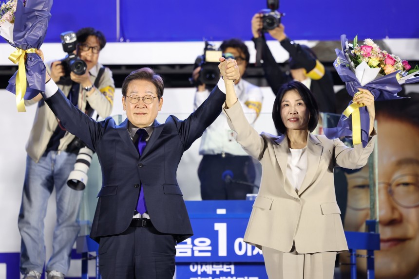 제21대 대통령 당선이 확실시되는 더불어민주당 이재명 대선 후보와 부인 김혜경 여사가 4일 서울 여의도 국회 인근에서 당 주최로 열린 국민개표방송 행사에 참석해 꽃다발을 받고서 시민들을 향해 두 팔을 들어올려 인사하